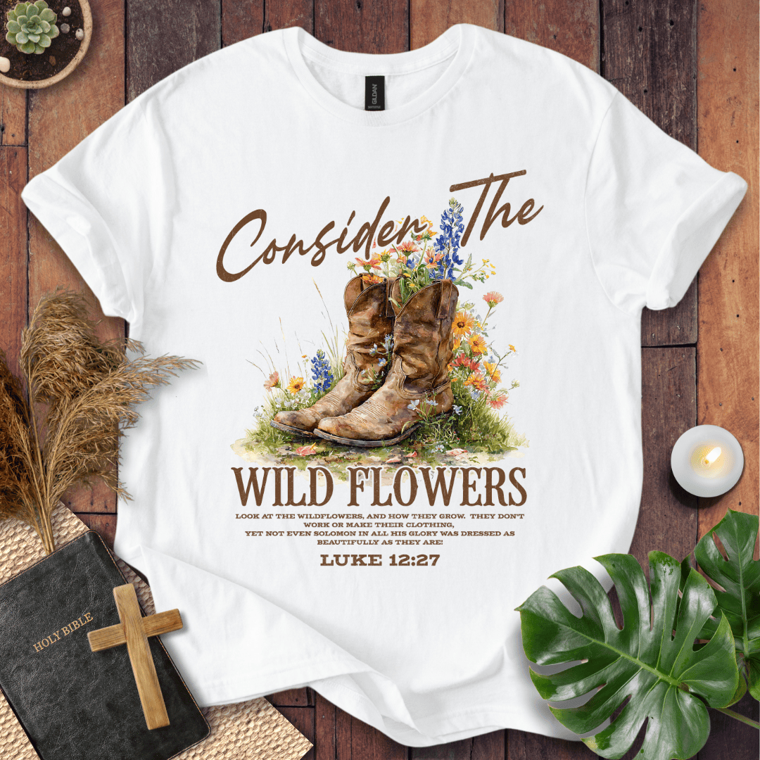 Western wildflower graphic tee with bible verse shirts text showing Luke 12:27 and boots on a natural cream shirt.