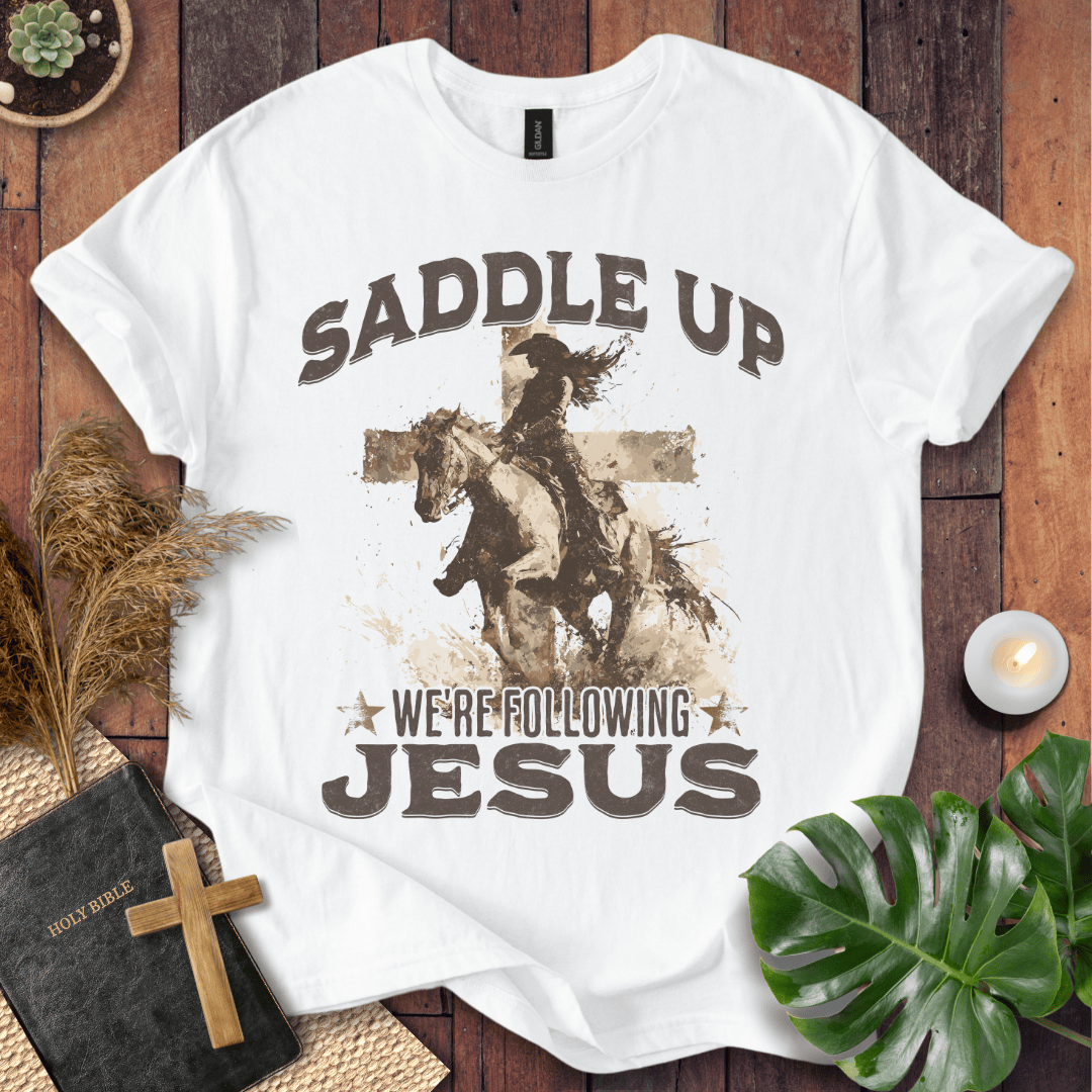 t-shirt featuring a cowgirl riding a horse in front of a cross with the text Saddle Up We're Following Jesus.