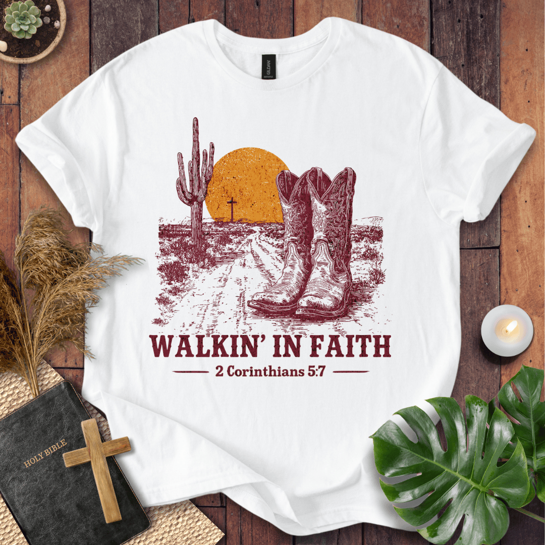 White t-shirt with cowboy boots and desert design on a wooden surface with decor items.