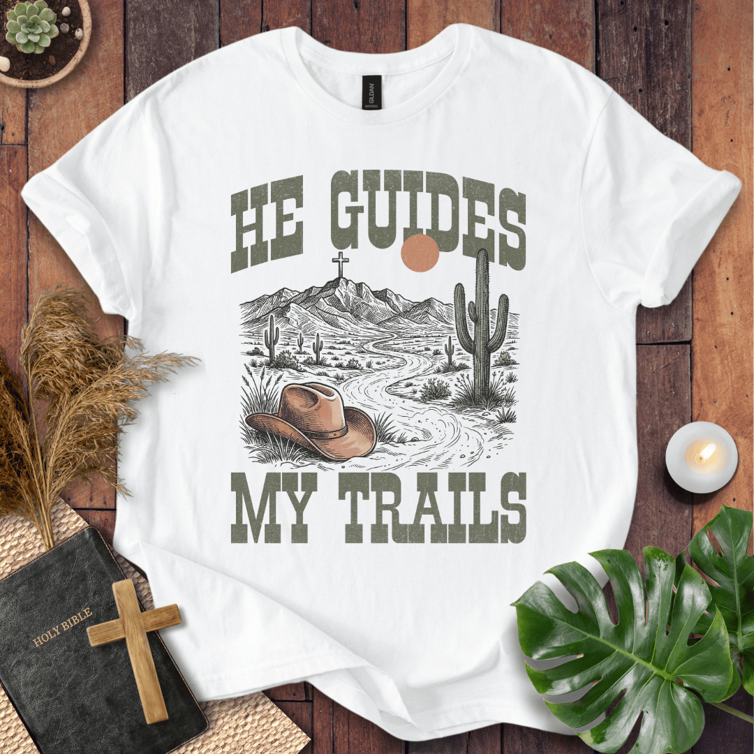 A Christian t-shirt with a desert landscape, cowboy hat, and cross, reading He Guides My Trails.